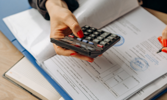 Zdjęcie przedstawiające osobe z kalkulatorem zapisującą obliczenia na kartce